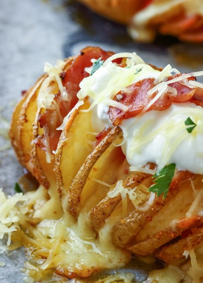 Loaded Hasselback Potato topped with sour cream and shredded cheese on a baking sheet lined with parchment paper
