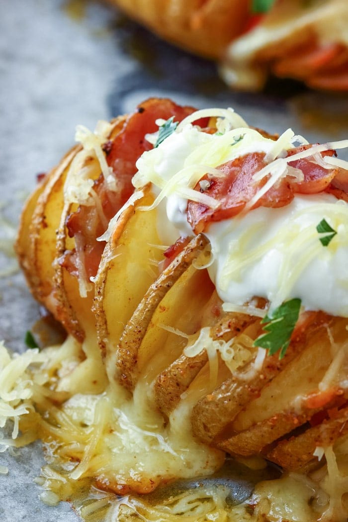Hasselback potato sliced with melted cheese bacon sour cream and parsley garnish on wax paper