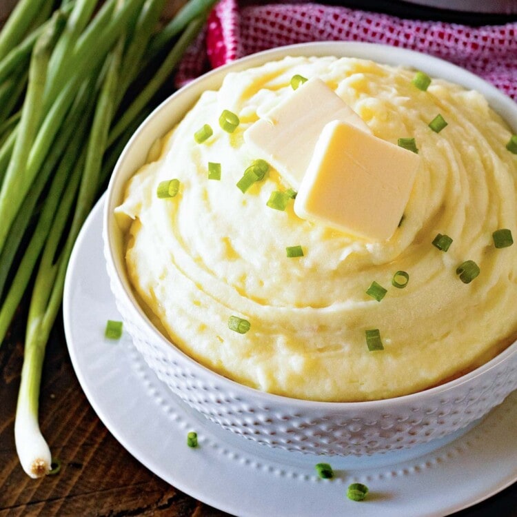 White bowl of mashed potatoes with two pads of butter on top sitting on a white plate in front of an instant po