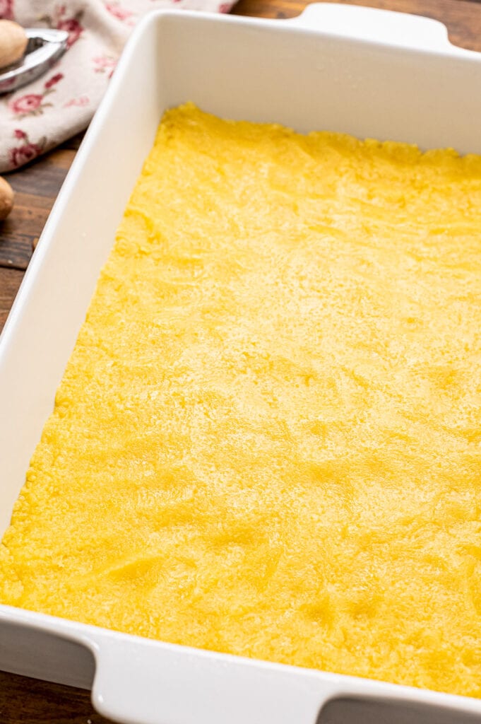 White baking dish with cake mix crust for pecan pie bars.