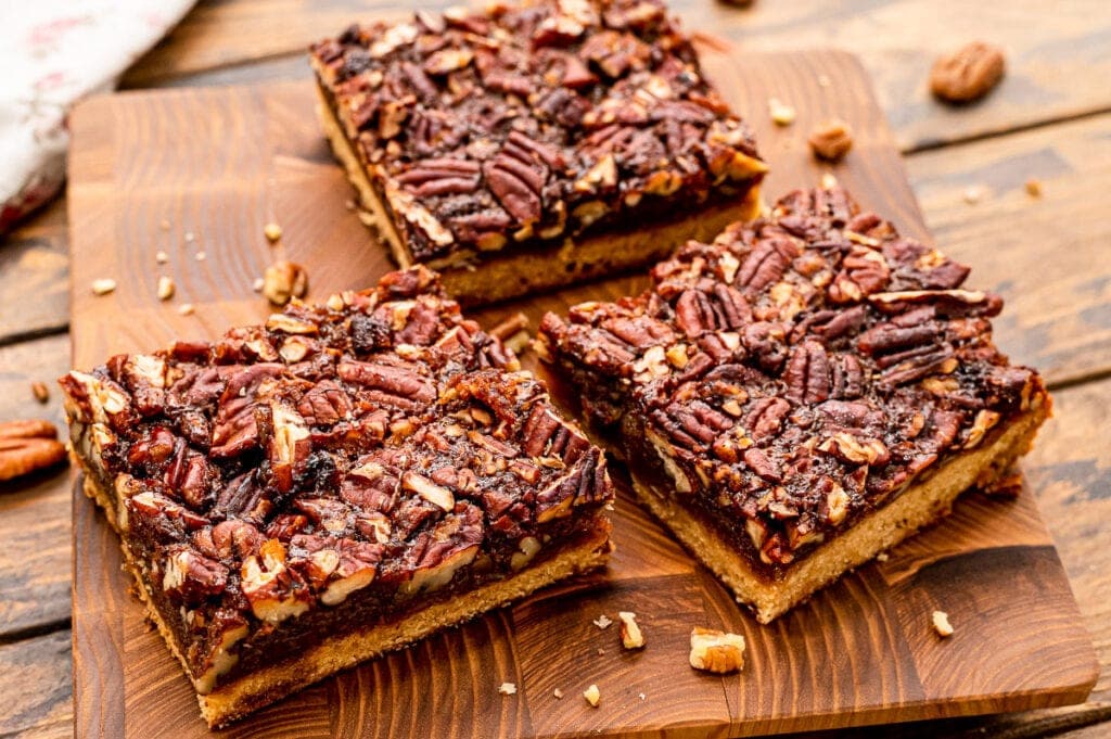 Three pecan pie bars on wooden cutting board