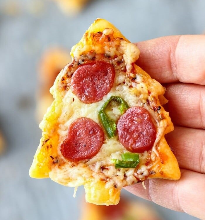 Hand holding a christmas tree mini pizza with pepperoni on it