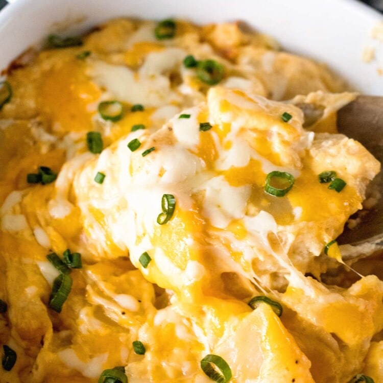 A wood spoon scooping out cheesy scalloped potatoes from a white baking dish