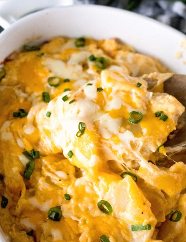 A wood spoon scooping out cheesy scalloped potatoes from a white baking dish