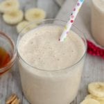 Glass of peanut butter banana smoothie with a polka dot straw on a table with banana slices, peanuts, and honey