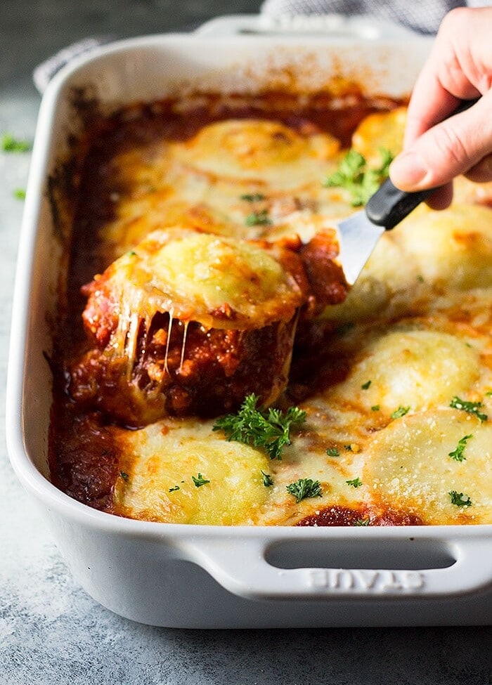 A spatula lifting a ravioli out of a white baking dish of ravioli lasagna