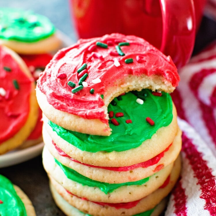 A stack of sugar cookies with red and green frosting next to a red mug and a red and white striped towel