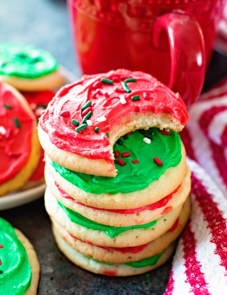 A stack of sugar cookies with red and green frosting next to a red mug and a red and white striped towel