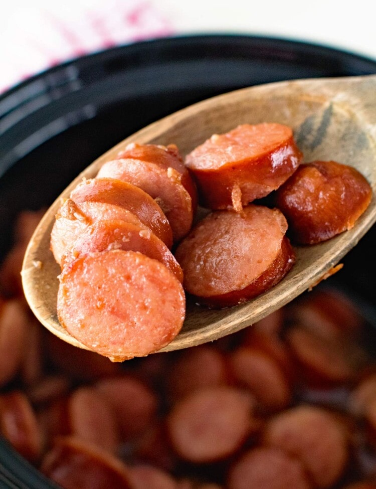 Crock Pot Glazed Kielbasa Bites on a wooden spoon being held over a crock pot