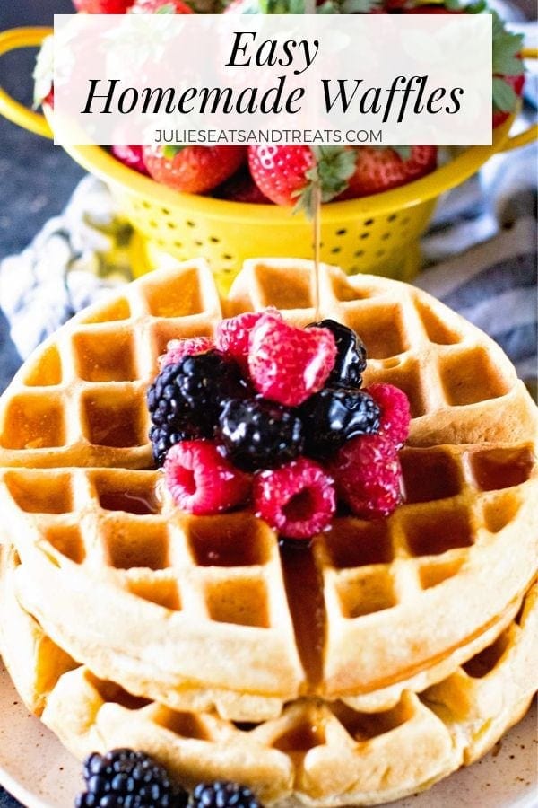 Syrup being poured over a stack of two waffles with berries on a plate