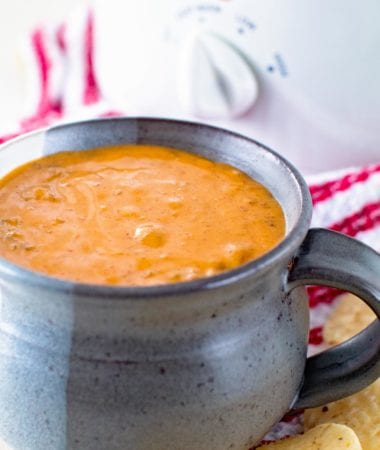 Quick and Easy Chili Cheese Dip in a gray mug in front of a white crock pot