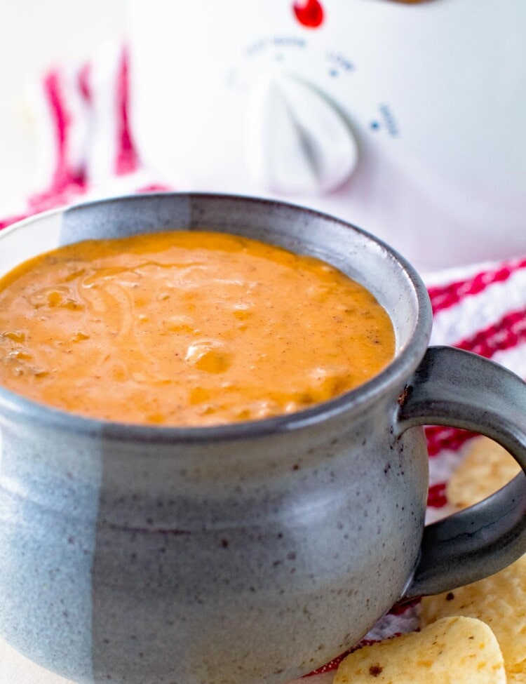 Quick and Easy Chili Cheese Dip in a gray mug in front of a white crock pot