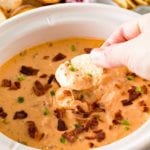 Hand dipping a chip into Slow Cooker Cheese Dip with Ranch and Chicken