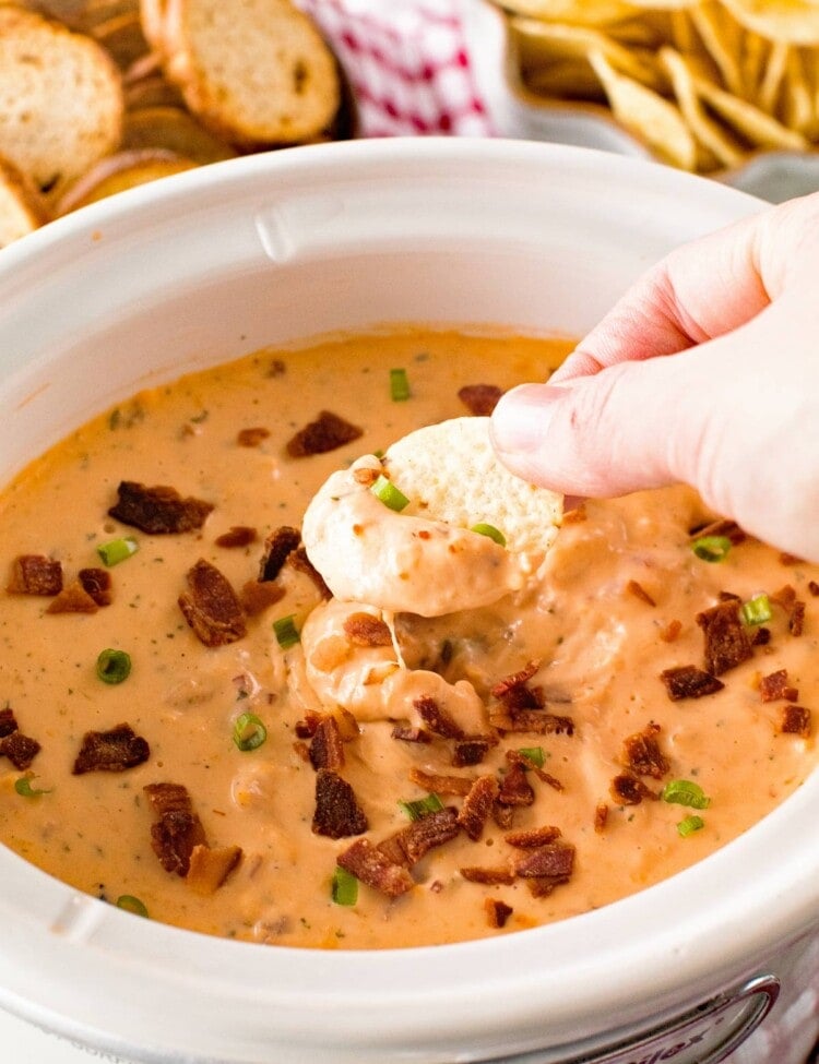 Hand dipping a chip into Slow Cooker Cheese Dip with Ranch and Chicken
