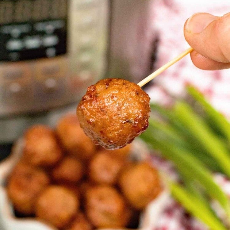 grape jelly meatball on a toothpick being held in front of a pressure cooker