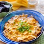 A blue bowl of mexican casserole topped with green onions