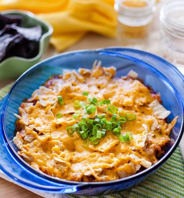 A blue bowl of mexican casserole topped with green onions