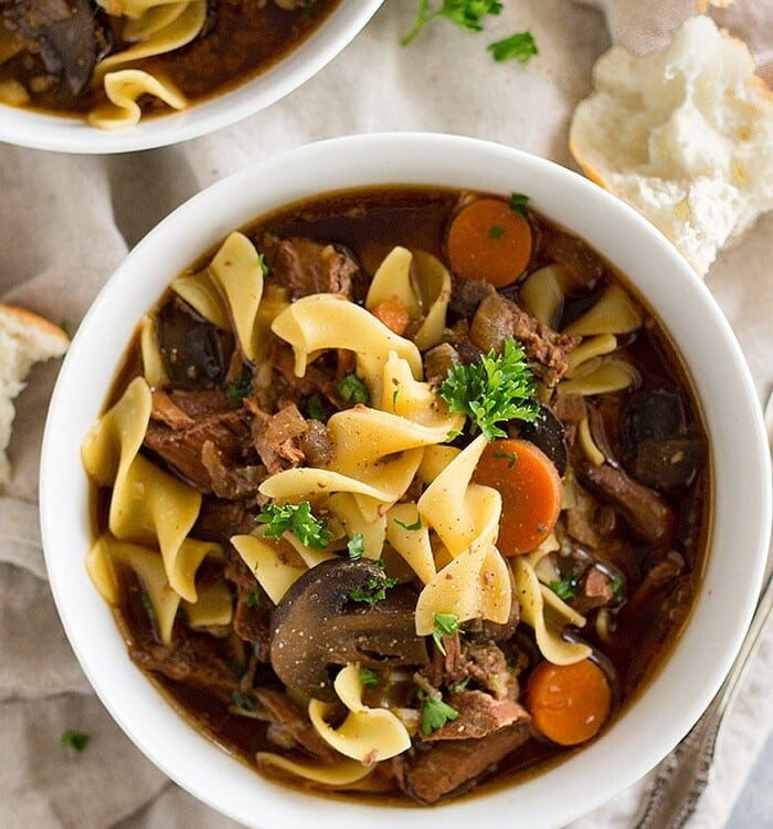slow cooker beef and noodle soup in two white bowls on a kitchen towel