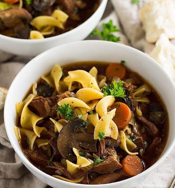 slow cooker beef and noodle soup in two white bowls on a kitchen towel