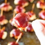 Hand holding a toothpick with a bbq bacon chicken bite on the end being held over a pan of more bbq bacon chicken bites