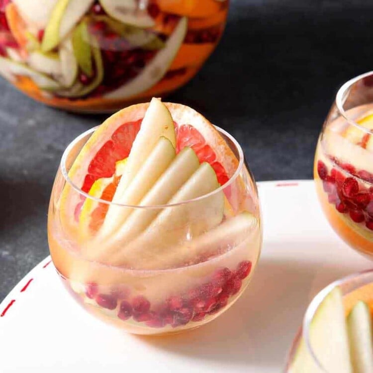 Three glasses of winter sangria on a white tray in front of a pitcher of sangria