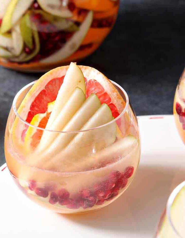 Three glasses of winter sangria on a white tray in front of a pitcher of sangria