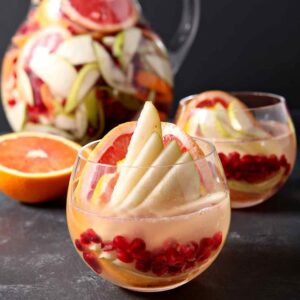 Two glasses and a pitcher of winter sangria on a stone counter