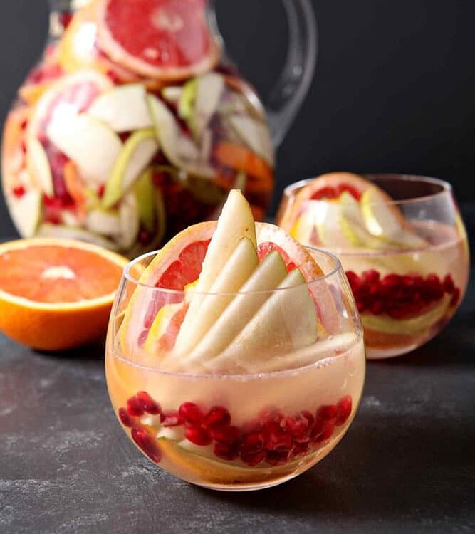 Two glasses and a pitcher of winter sangria on a stone counter