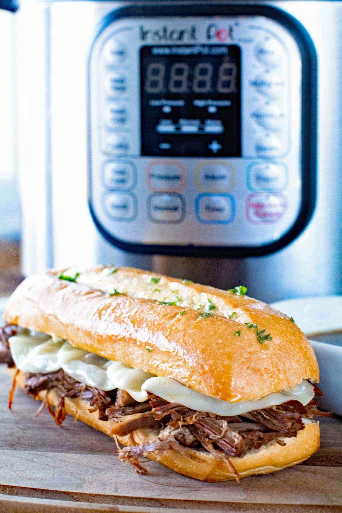 Wood cutting board with french dip sandwich on it with instant pot in background