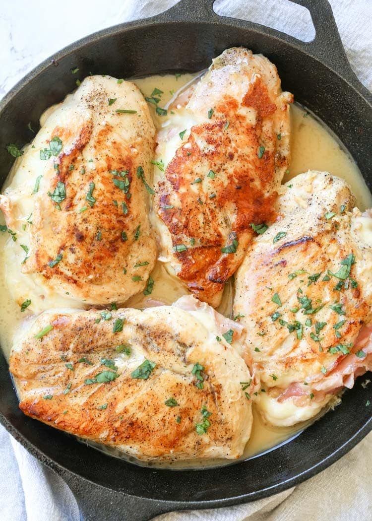 Overhead image of stuffed chicken breasts and sauce in a cast iron skillet