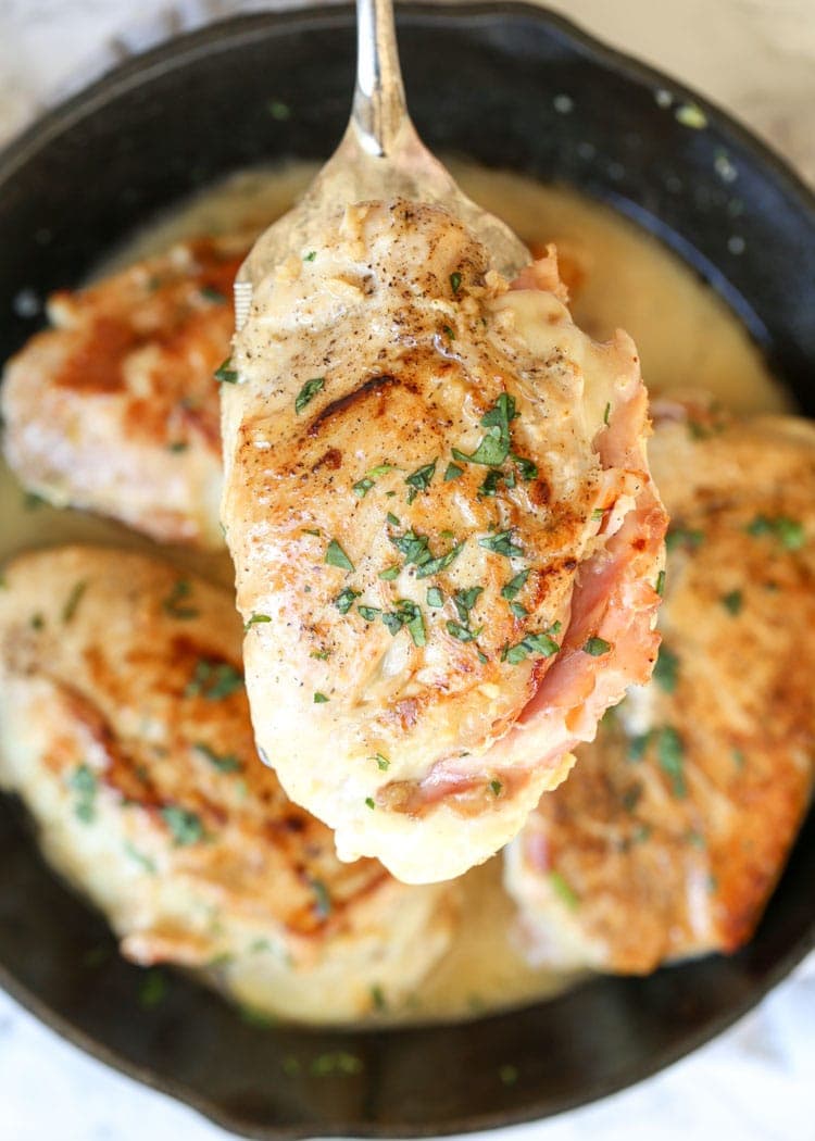 Stuffed chicken breast on spoon with cast iron skillet in background with more chicken breasts