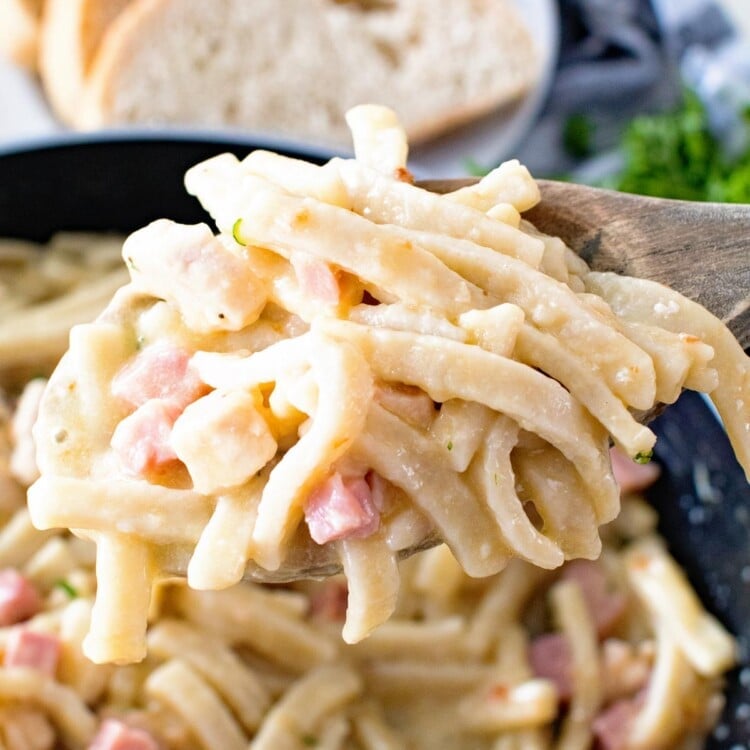 Chicken Cordon Bleu Noodle skillet on a wooden spoon being held over a skillet of pasta