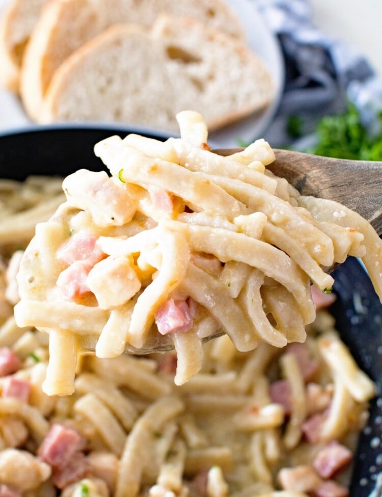 Chicken Cordon Bleu Noodle skillet on a wooden spoon being held over a skillet of pasta