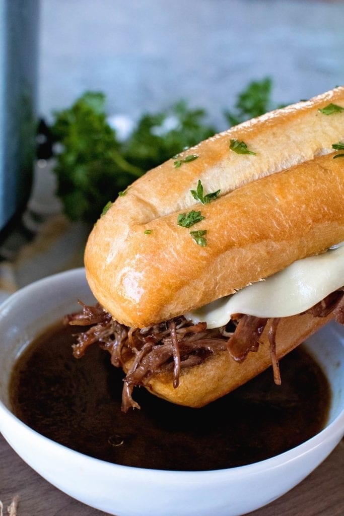 French Dip Sandwich being dipped into a white bowl holding Au Jus