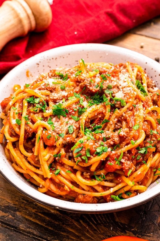 Bowl of spaghetti garnished with parmesan cheese and chopped parsley.