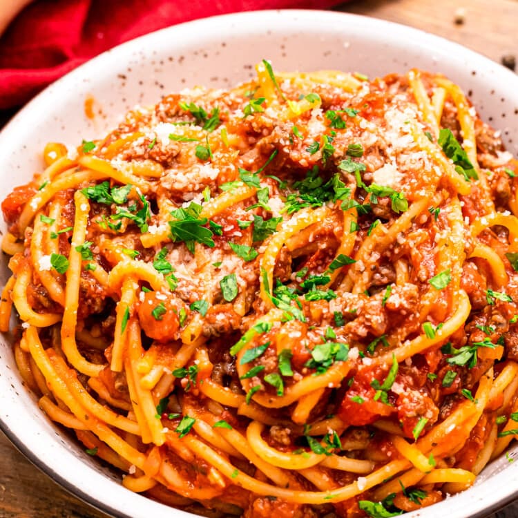 Bowl of spaghetti garnished with parmesan cheese and chopped parsley.