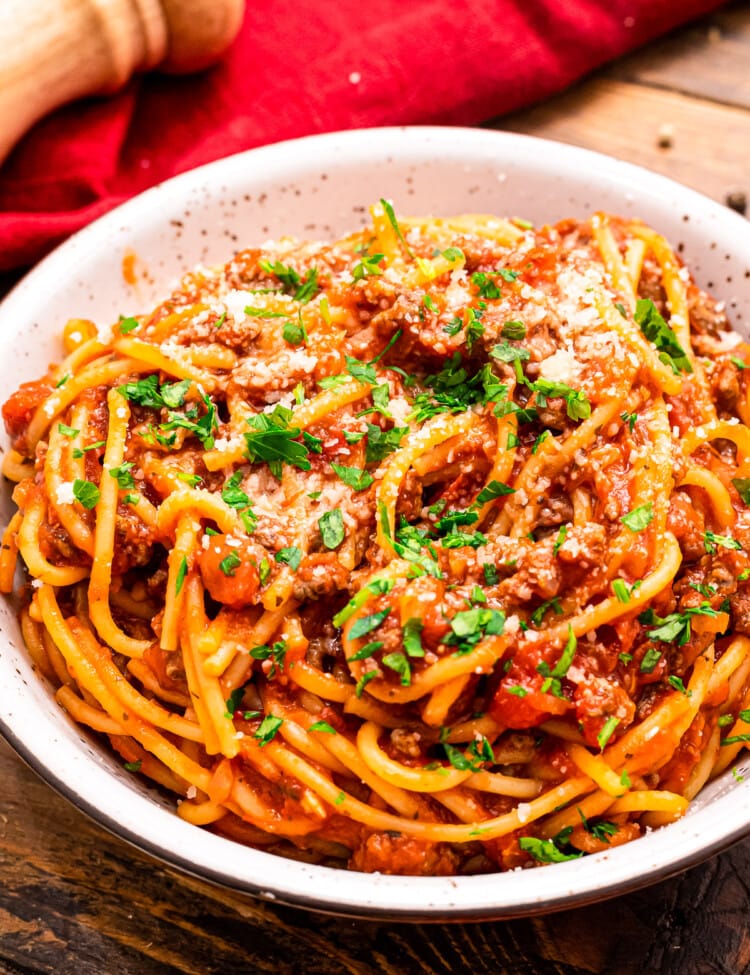 Bowl of spaghetti garnished with parmesan cheese and chopped parsley.