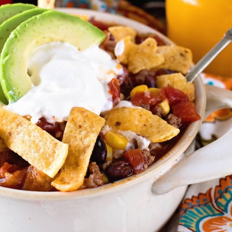 Taco Soup in a white bowl topped with fritos, sour cream, and avocado slices