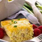 A piece of sausage cheese hash brown breakfast casserole on a white square plate with a fork and raspberries