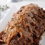 French Onion Meatloaf, sitting on a white platter, covered in gruyere gravy