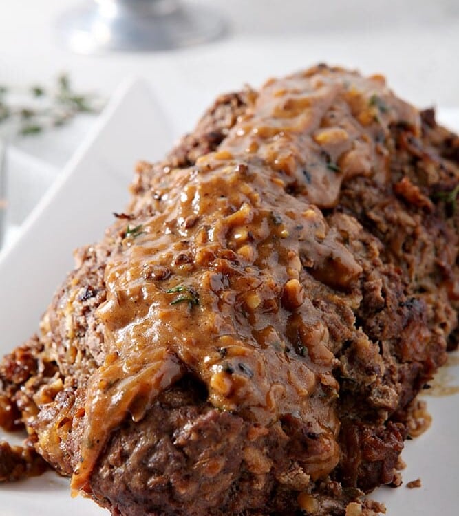 French Onion Meatloaf, sitting on a white platter, covered in gruyere gravy