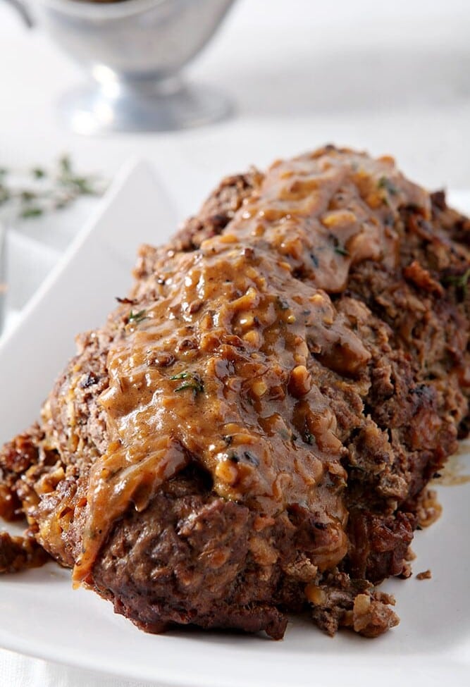 French Onion Meatloaf, sitting on a white platter, covered in gruyere gravy