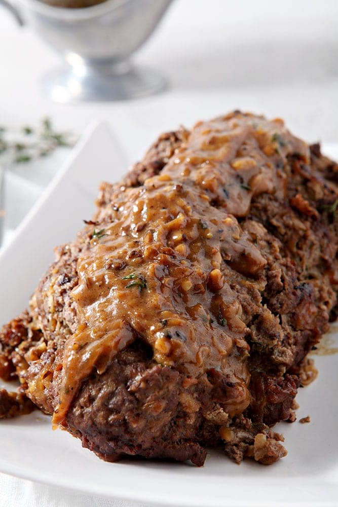 French Onion Meatloaf, sitting on a white platter, covered in gruyere gravy