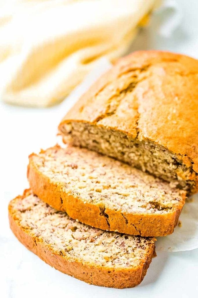 A loaf of banana bread with two slices laying in front of it.
