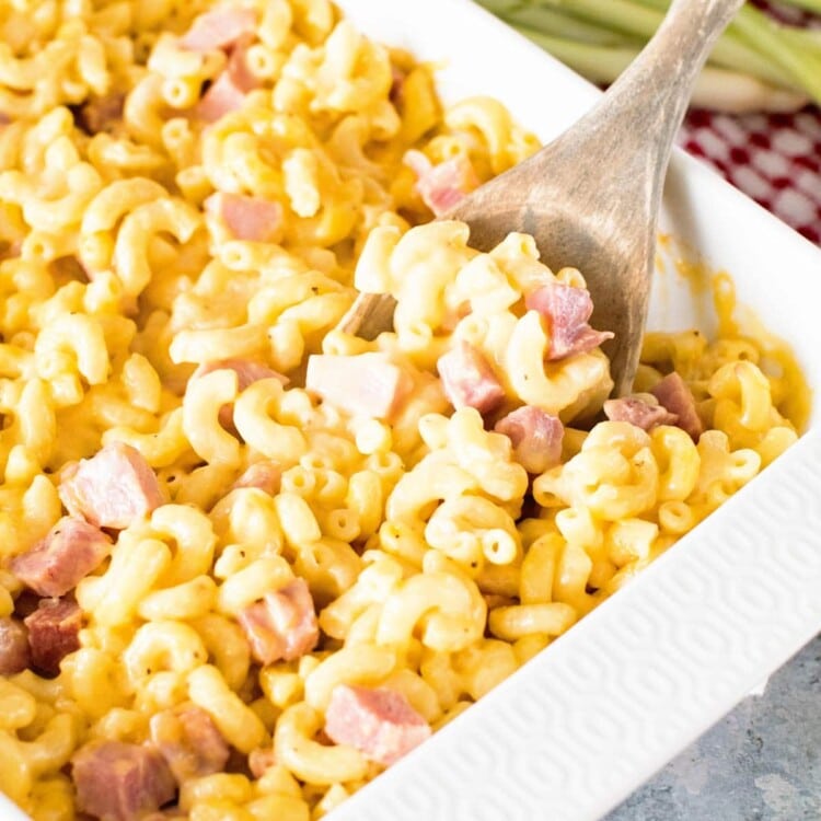 ham and cheese casserole with noodles in a white baking dish with a wood spoon in it