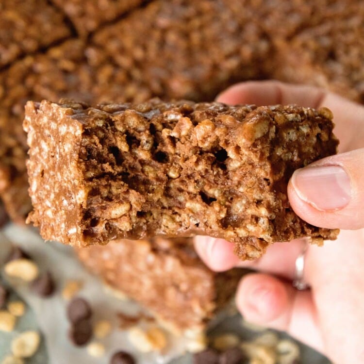 A hand holding a chocolate peanut butter rice krispie with a bite out of it