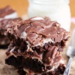 Three fudgy marshmallow brownies stacked next to a fork and a glass jar of milk