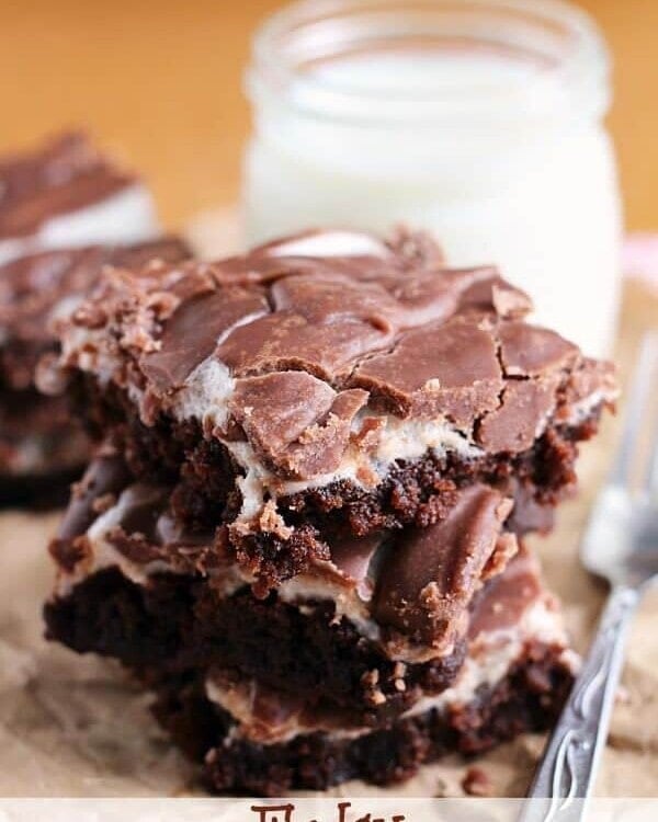 Three fudgy marshmallow brownies stacked next to a fork and a glass jar of milk