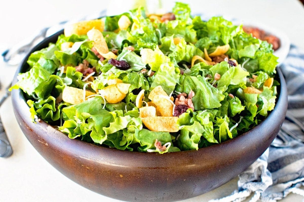 Landscape photo of Lettuce Frito Salad in brown wooden bowl with linen napkin in background