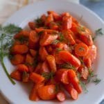 Roasted Carrots with dill on a white plate sitting on a yellow cloth napkin